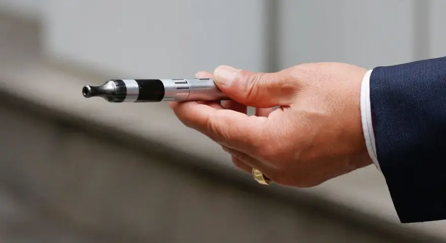 Mano con traje sosteniendo un cigarrillo electrónico, listo para vapear en el trabajo.