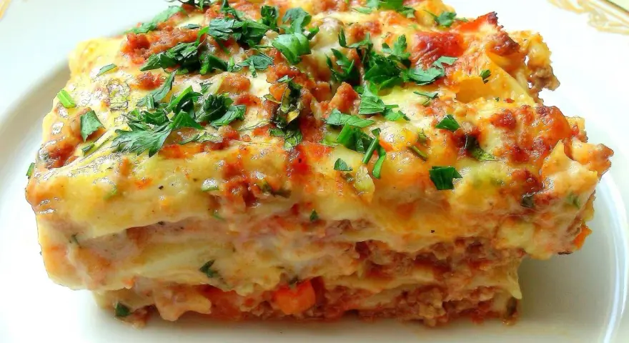 Pyszna lasagne Ani Starmach, z warstwami mięsa, sosu i sera, posypana świeżą natką pietruszki.