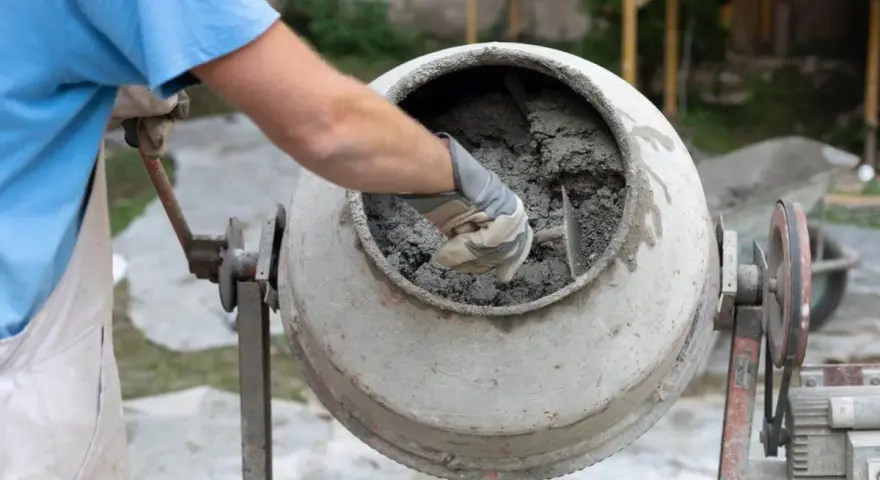 Mieszanie betonu w betoniarce. Pracownik w rękawicach sprawdza konsystencję, zastanawiając się, ile cementu na metr sześcienny betonu potrzeba do uzyskania idealnej mieszanki.