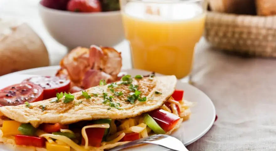Pyszne śniadanie bez chleba: omlet z warzywami i serem, bekon, pomidory, truskawki i sok pomarańczowy.