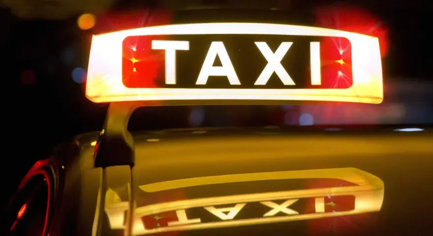 Leuchtendes TAXI-Schild mit roten Blinklichtern, das einen Taxi-Alarm signalisiert. Die Reflexion auf dem dunklen Auto verstärkt die nächtliche Atmosphäre.