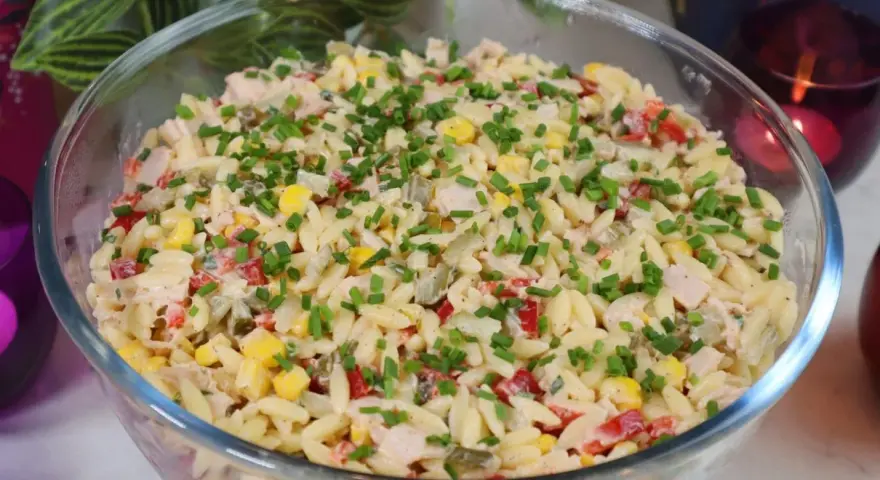 Pyszna sałatka z makaronem orzo, kukurydzą, papryką i kurczakiem, posypana szczypiorkiem. Idealna na letnie dni.
