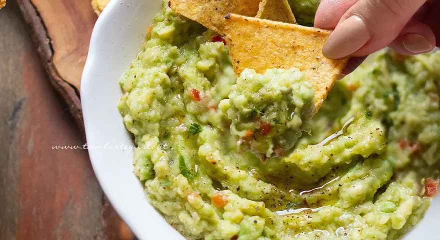 Un chip di mais raccoglie il cremoso guacamole, mostrando come fare il guacamole fresco e delizioso.