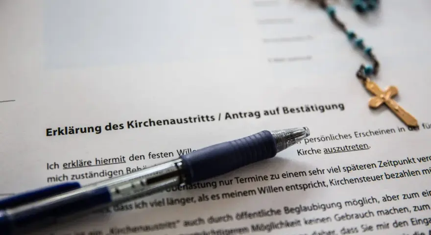 Dokument zur Kirchenaustrittserklärung mit Stift und Rosenkranz. Der Text erwähnt "Kirchensteuer bezahlen", was auf eine mögliche Kirchensteuererstattung hindeutet.