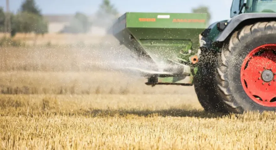 Traktor rozsiewa wapno magnezowe na polu.