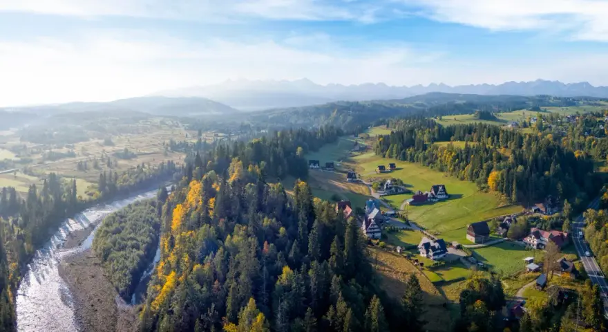 Widok z lotu ptaka na Bukowinę Tatrzańską z górami w tle, rzeką i lasami.