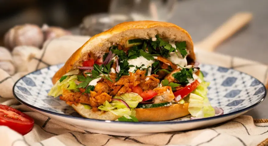Pyszny, domowy kebab z kurczaka z piekarnika, pełen świeżych warzyw i sosu, na ozdobnym talerzu.