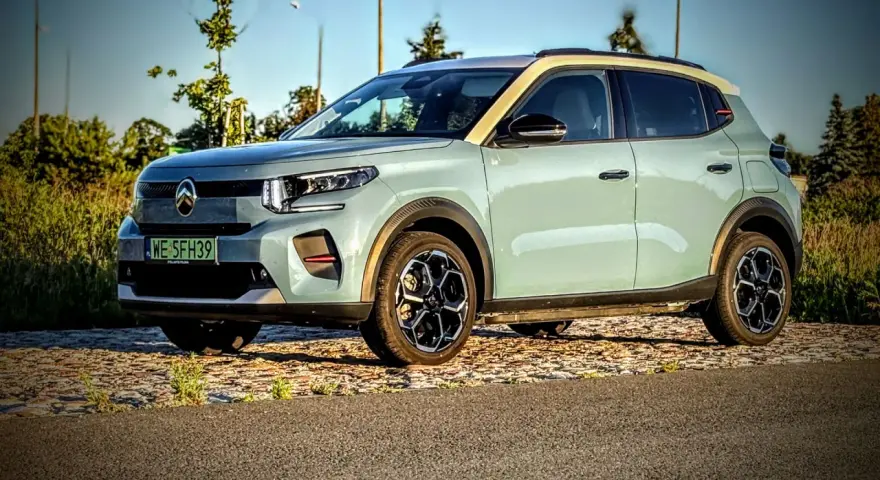 Jasnoszary Citroën ë-C3 z żółtym dachem stoi na tle drzew i nieba.