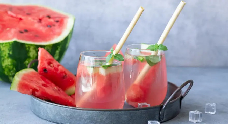 Orzeźwiający drink z arbuzem i miętą, podany na tacy z kawałkami arbuza i kostkami lodu. Idealny na upalne dni.