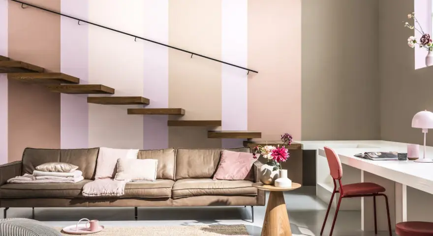 Un confortable canapé en cuir marron est installé sous un escalier flottant en bois. La pièce est décorée de coussins roses et d'un tapis en jute.