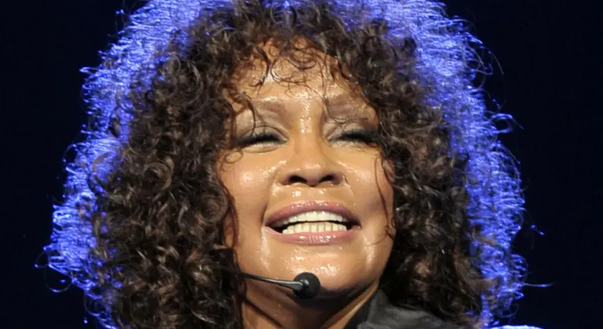 Whitney Houston z zamkniętymi oczami, w pełni emocji, pokazuje niesamowitą **skalę głosu**.