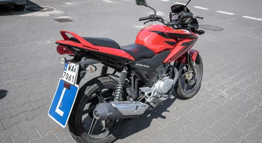 Czerwony motocykl Honda CBF125 z tablicą "L" i numerem rejestracyjnym WA7 7061, gotowy do nauki jazdy na prawo jazdy a1.