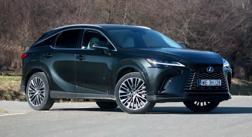 Ciemnozielony Lexus 450h z eleganckimi felgami stoi na drodze, otoczony suchymi krzewami.