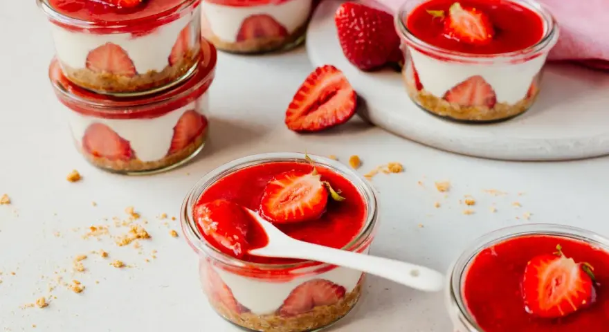 Mehrere kleine Gläser mit einem cremigen Dessert mit Erdbeeren und einer roten Erdbeersauce.