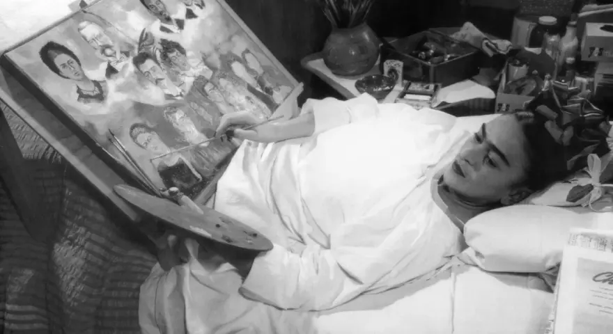 Frida Kahlo målar i sängen, omgiven av sina porträtt av familj och vänner, kanske sina syskon.