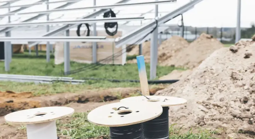 Na placu budowy paneli słonecznych przygotowywane są kable do uziemienia. Widać szpule z przewodami i metalowe konstrukcje.