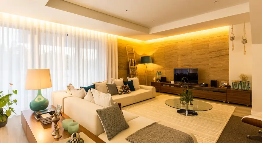 Salón moderno con sofá blanco, mesa de centro de cristal y **luz indirecta** que ilumina la pared de piedra y las cortinas.