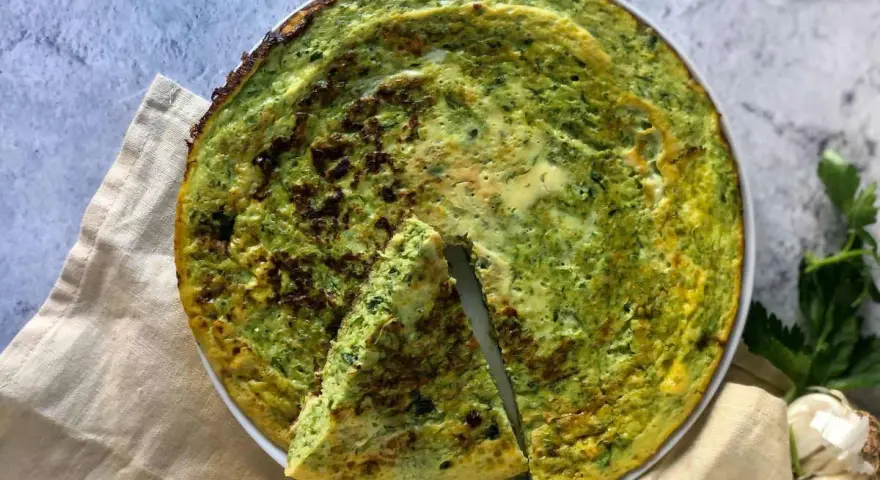 Frittata di zucchine in padella, dorata e profumata, con una fetta tagliata per mostrare la morbidezza interna.