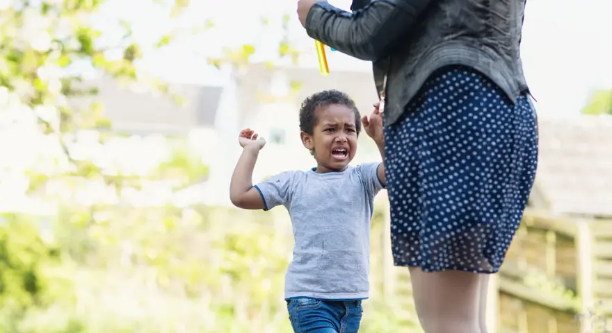 Ein 3-jähriges Kind hat einen Wutanfall, während eine Person Seifenblasen macht.