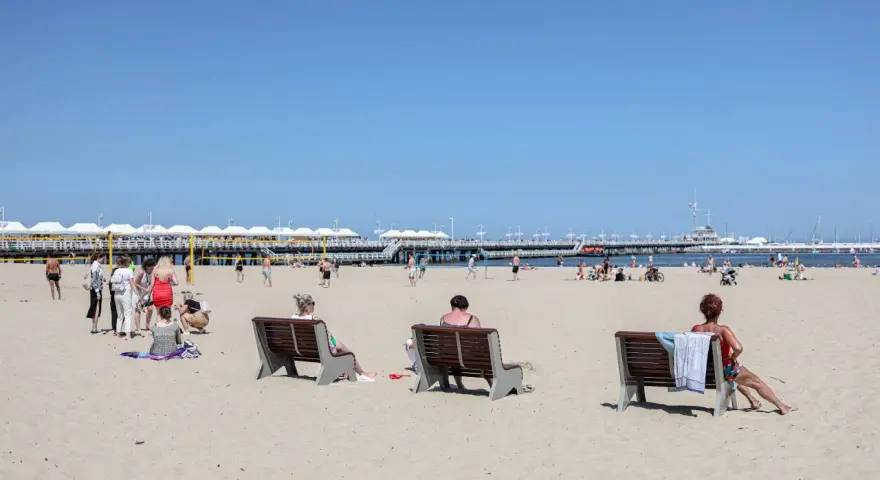 Ludzie odpoczywają na plaży, ciesząc się słońcem i widokiem na molo. To idealne miejsce na polską riwierę.