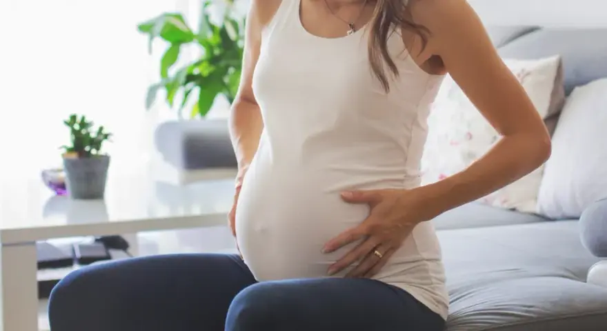 Kobieta w ciąży siedzi na kanapie, dotykając brzucha. Zauważyła brązowe plamienie w ciąży, co ją martwi.