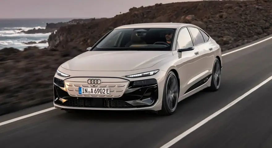 Jasnoszary Audi A6 e-tron jedzie po drodze z widokiem na ocean i góry.