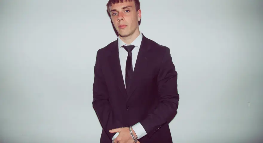 Młody mężczyzna w czarnym garniturze i białej koszuli, z krawatem. Kinny Zimner prezentuje się elegancko.