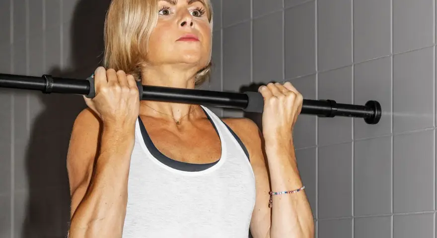 En kvinna med blont hår utför chin ups vid en stång.
