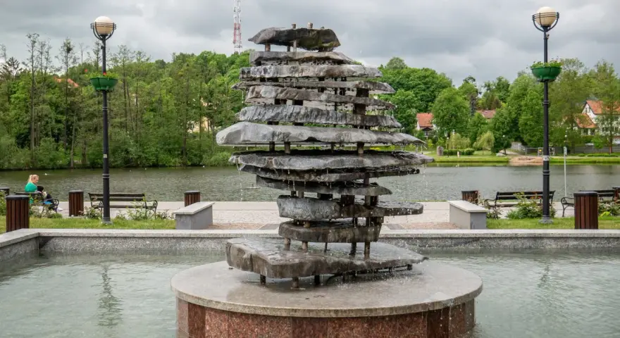 Kamienna rzeźba-fontanna nad jeziorem, jedna z atrakcji Czosu. W tle drzewa i budynki.