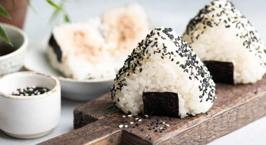 Trójkątne onigiri sushi z czarnym sezamem i kawałkiem nori na drewnianej desce.