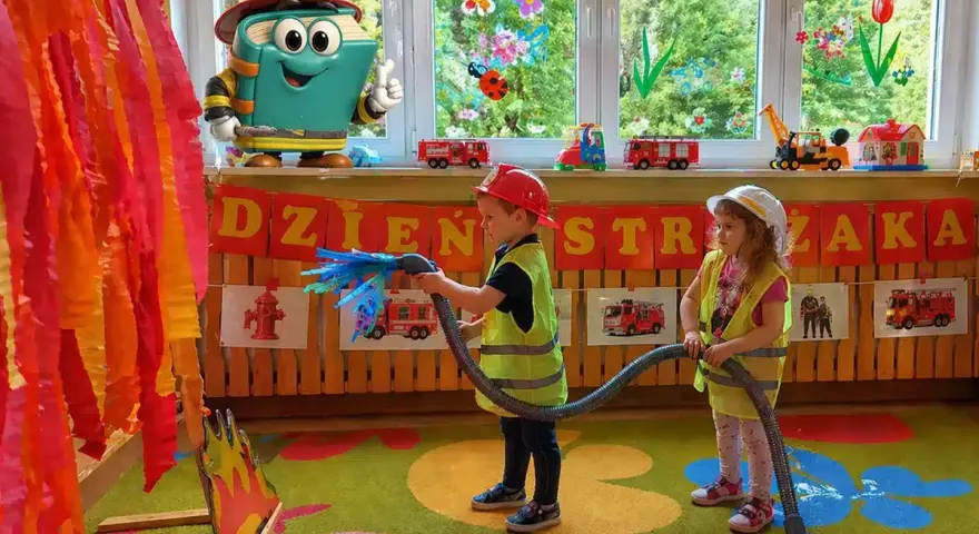 Dzieci gaszą pożar, świetne pomysły na dni otwarte w przedszkolu! Maskotka-książka w stroju strażaka zachęca do zabawy.