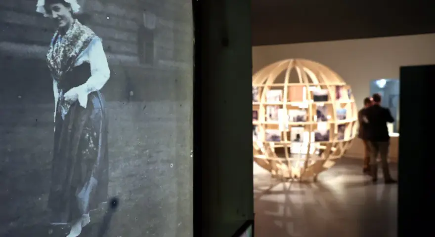 Exposition Albert Kahn : une femme en costume traditionnel sur une photo ancienne, un globe de bois rempli de clichés en arrière-plan.