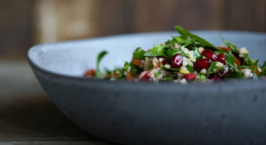 Frischer Tabouleh-Salat mit Granatapfelkernen in einer grauen Schüssel. Ein köstliches Rezept für den Sommer.