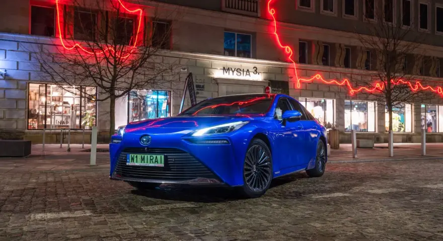 Niebieska Toyota Mirai na nocnej ulicy z neonowym oświetleniem.