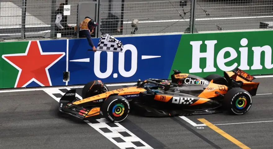 El coche de McLaren cruza la meta en el **Gran Premio Países Bajos**. El piloto celebra la victoria ondeando la bandera a cuadros.