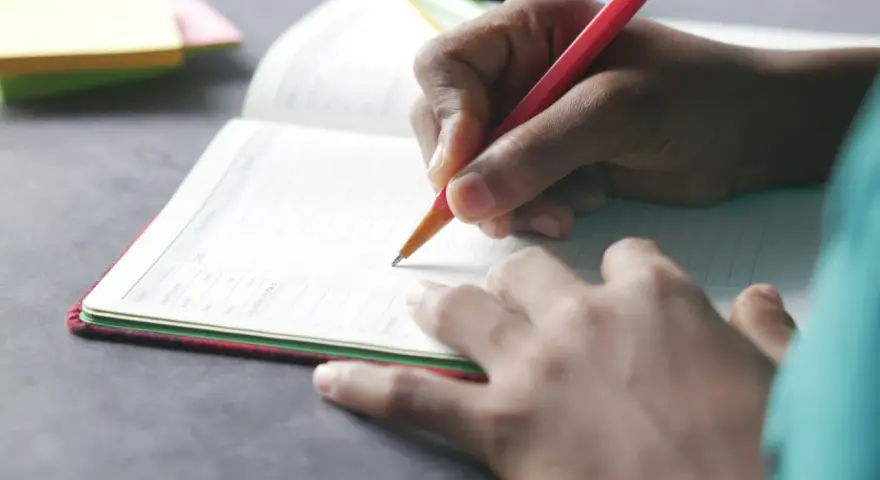 Dłoń pisze w zeszycie, co to dysgrafia? Trudności z pisaniem mogą dotyczyć każdego.