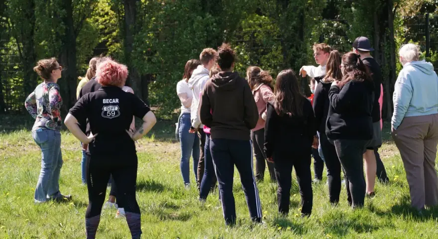 Groupe de jeunes adultes debout dans un champ verdoyant, certains se regardent.