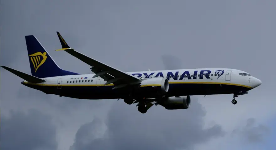 Samolot Ryanair z logo na ogonie leci na tle pochmurnego nieba. Może to być symbol zmiany nazwiska, gdy pasażerowie zmieniają swoje dane przed podróżą.