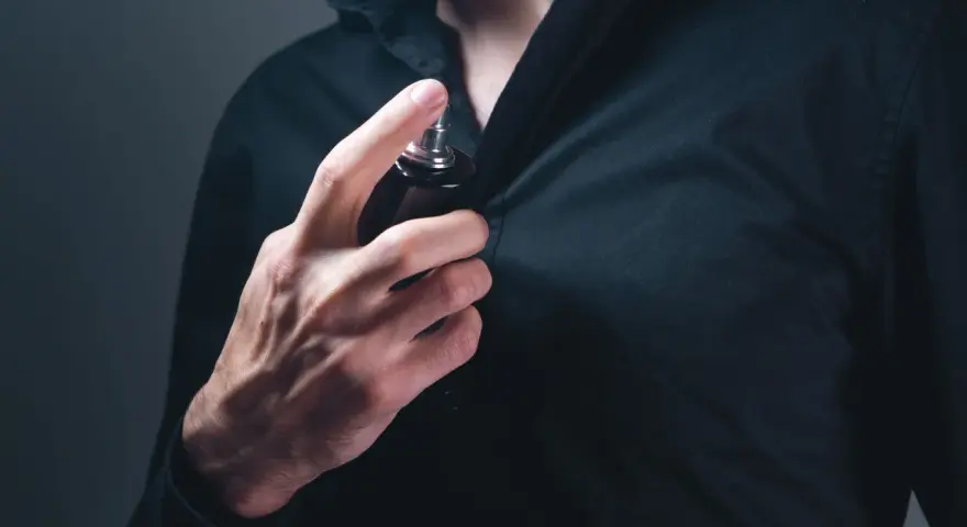 Mann sprüht sich Parfum auf die Brust.