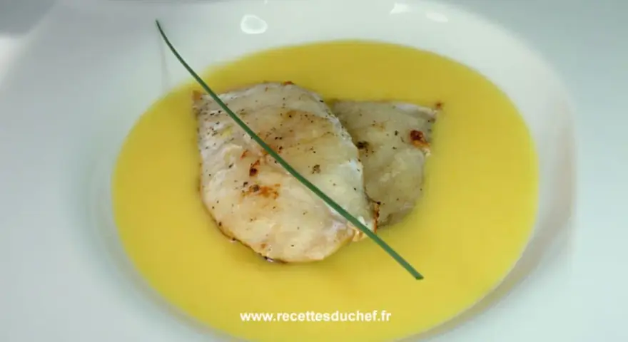 Deux filets de poisson poêlés reposent dans une onctueuse sauce à l'orange, décorés d'une tige de ciboulette.
