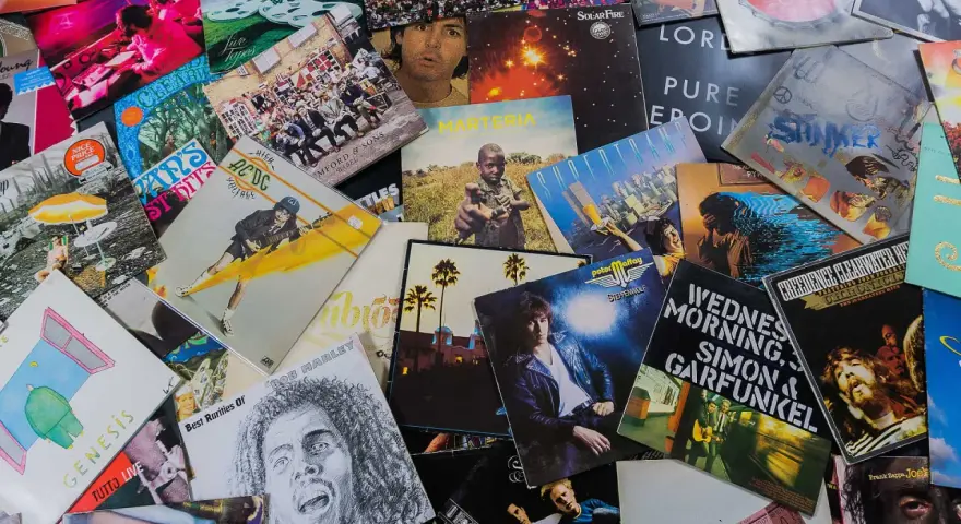Eine bunte Sammlung von Schallplatten zeigt, welche Musikarten es gibt: Rock von AC/DC, Pop von Genesis, Folk von Simon & Garfunkel und Reggae von Bob Marley.