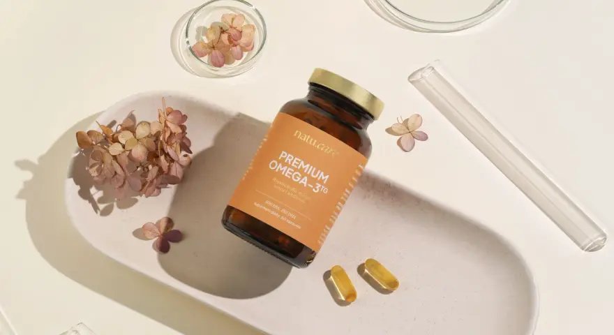 Suplement Omega-3 z DHA dla kobiet w ciąży, wspierający rozwój mózgu dziecka. Na zdjęciu buteleczka i kapsułki na tle suszonych kwiatów.