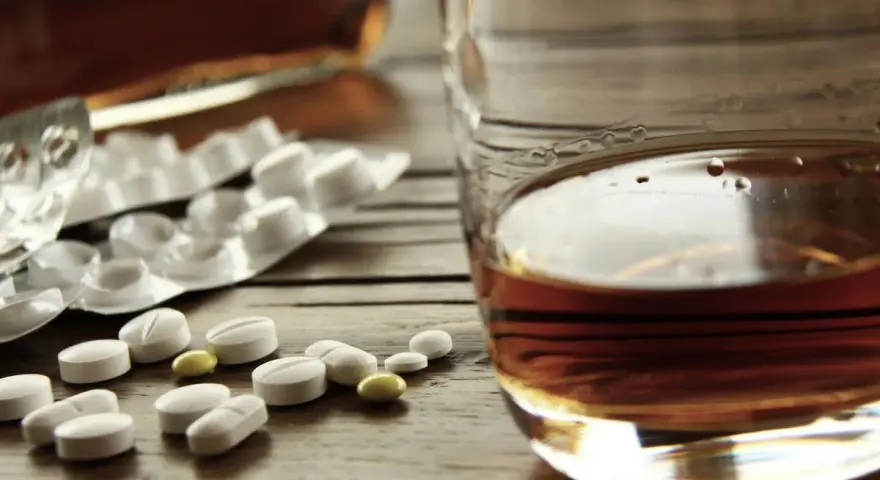 Tabletki i szklanka z alkoholem. Zastanawiasz się, po jakim czasie od zastrzyku można pić alkohol? To ważne pytanie.