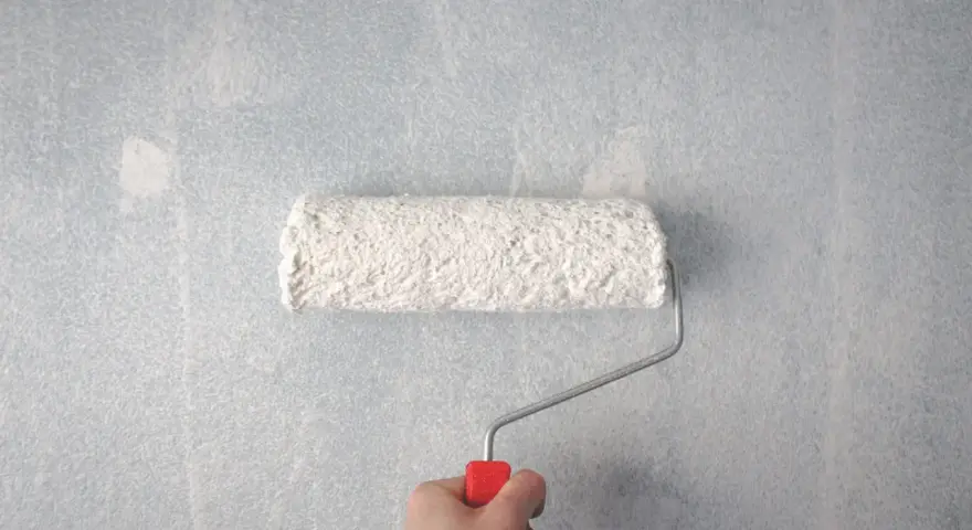 En hand håller en färgroller med vitt spackel för att jämna ut en tapet.