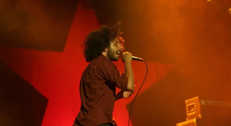 Zac Zack de la Rocha śpiewa z pasją na koncercie Rage Against the Machine. Czerwona gwiazda w tle podkreśla energię występu.