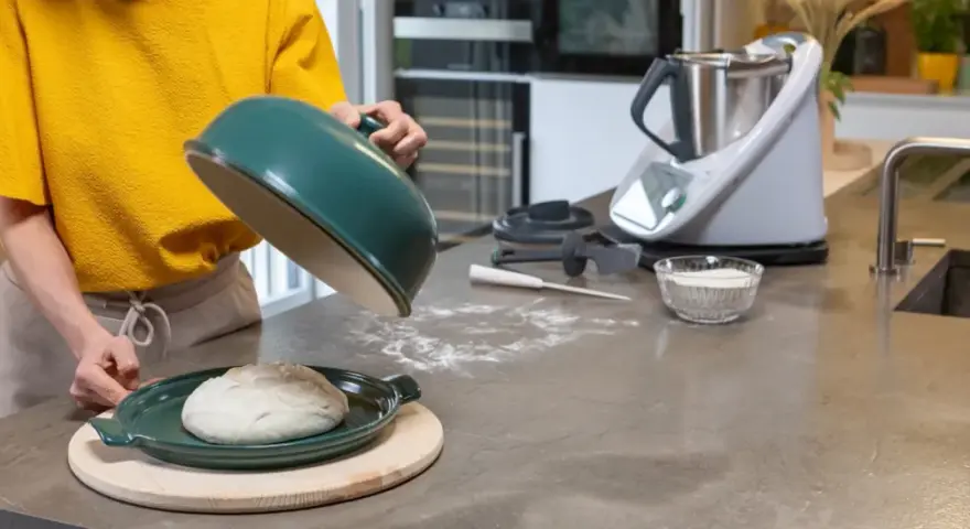 Préparation de la pâte à pizza avec un robot culinaire. Une boule de pâte repose sur un plat vert, prête à être cuite.