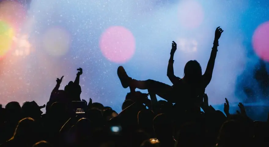 Tłum na jednym z największych festiwali muzycznych na świecie. Kobieta na rękach, ręce w górze, światła sceny.