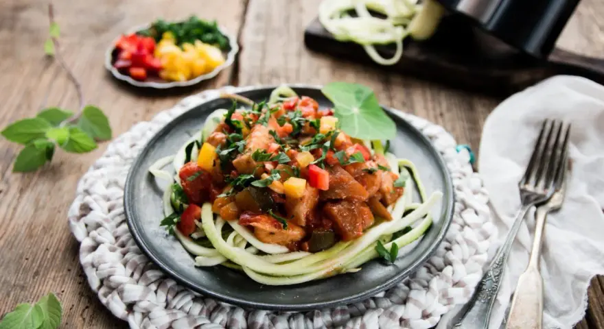 Spaghetti z cukinii z kurczakiem i warzywami w sosie na talerzu.