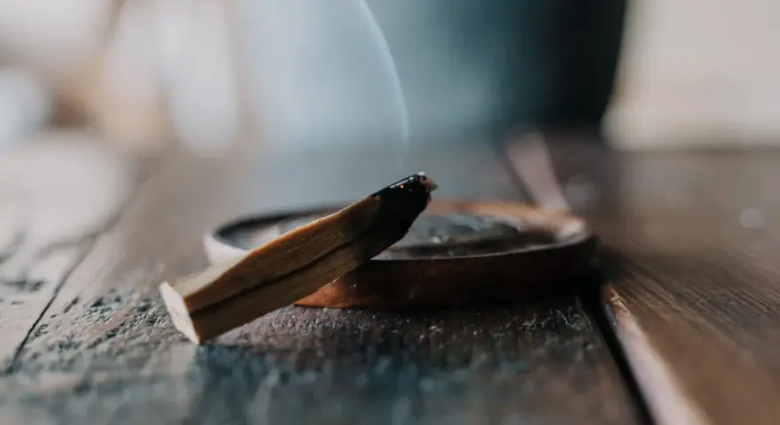 Un palo santo humeante sobre un plato de madera, parte de un ritual de limpieza.