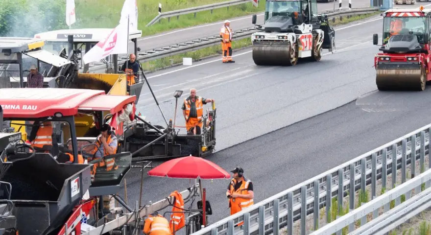Arbeiter legen auf der ADAC A2 mit Maschinen und Walzen neuen Asphalt.